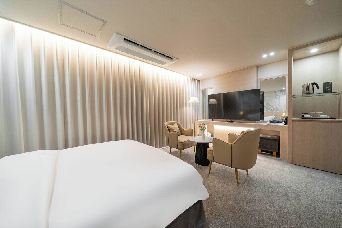 A hotel room with a large bed, a TV, a desk with a chair, and a sofa.