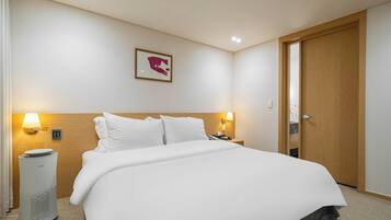 Habitación de hotel con una cama, dos lámparas de noche, un cuadro en la pared, una puerta de madera y un calentador portátil.