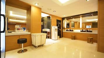 A modern hotel bathroom with a large mirror, a sink, a toilet, and a small stool.
