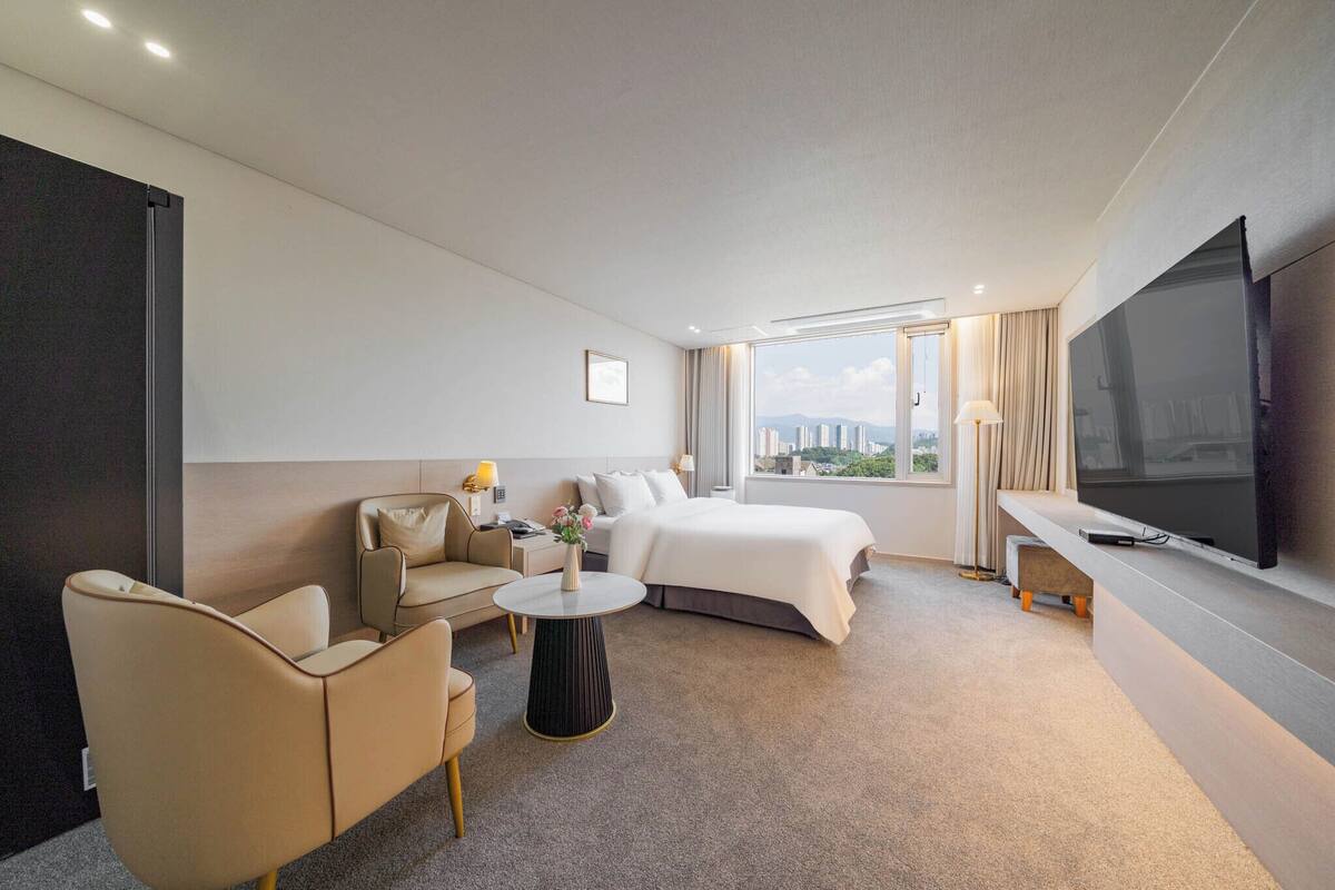 A modern hotel room with a bed, a sofa, a coffee table, and a TV.