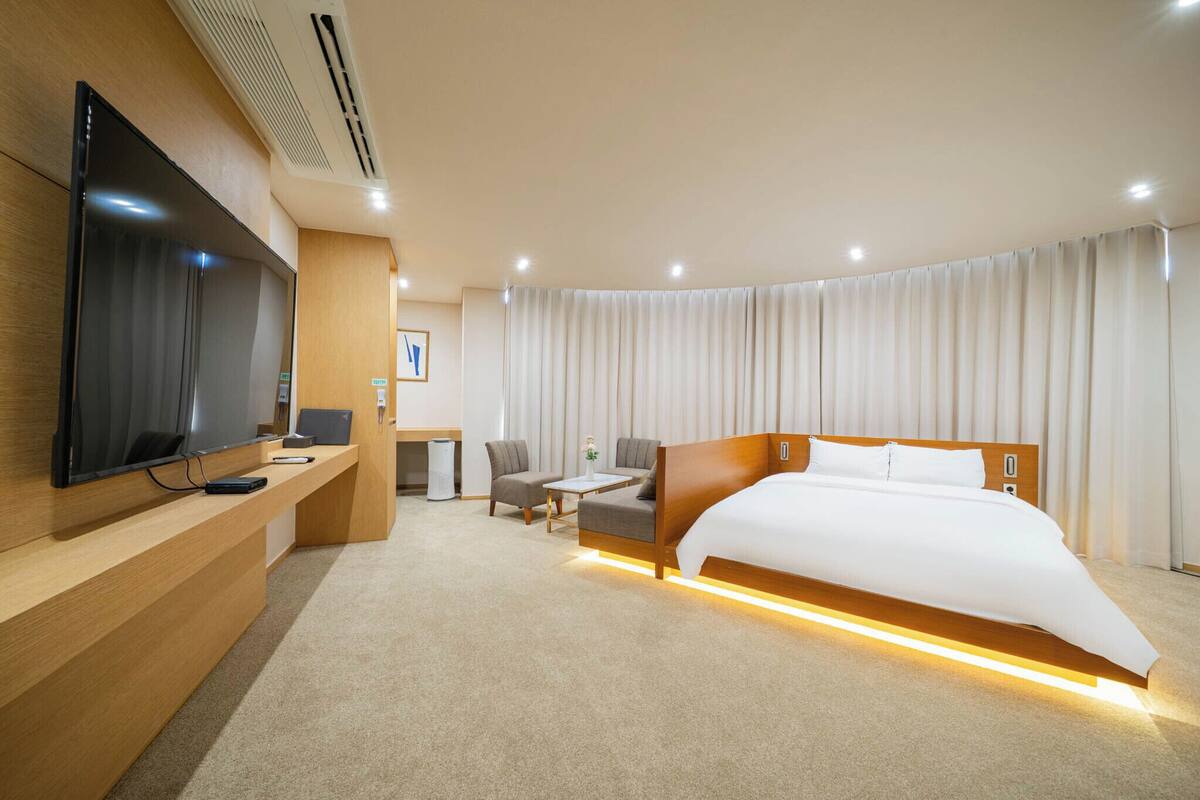 A modern hotel room with a large bed, a flat-screen TV, a desk, and a seating area.
