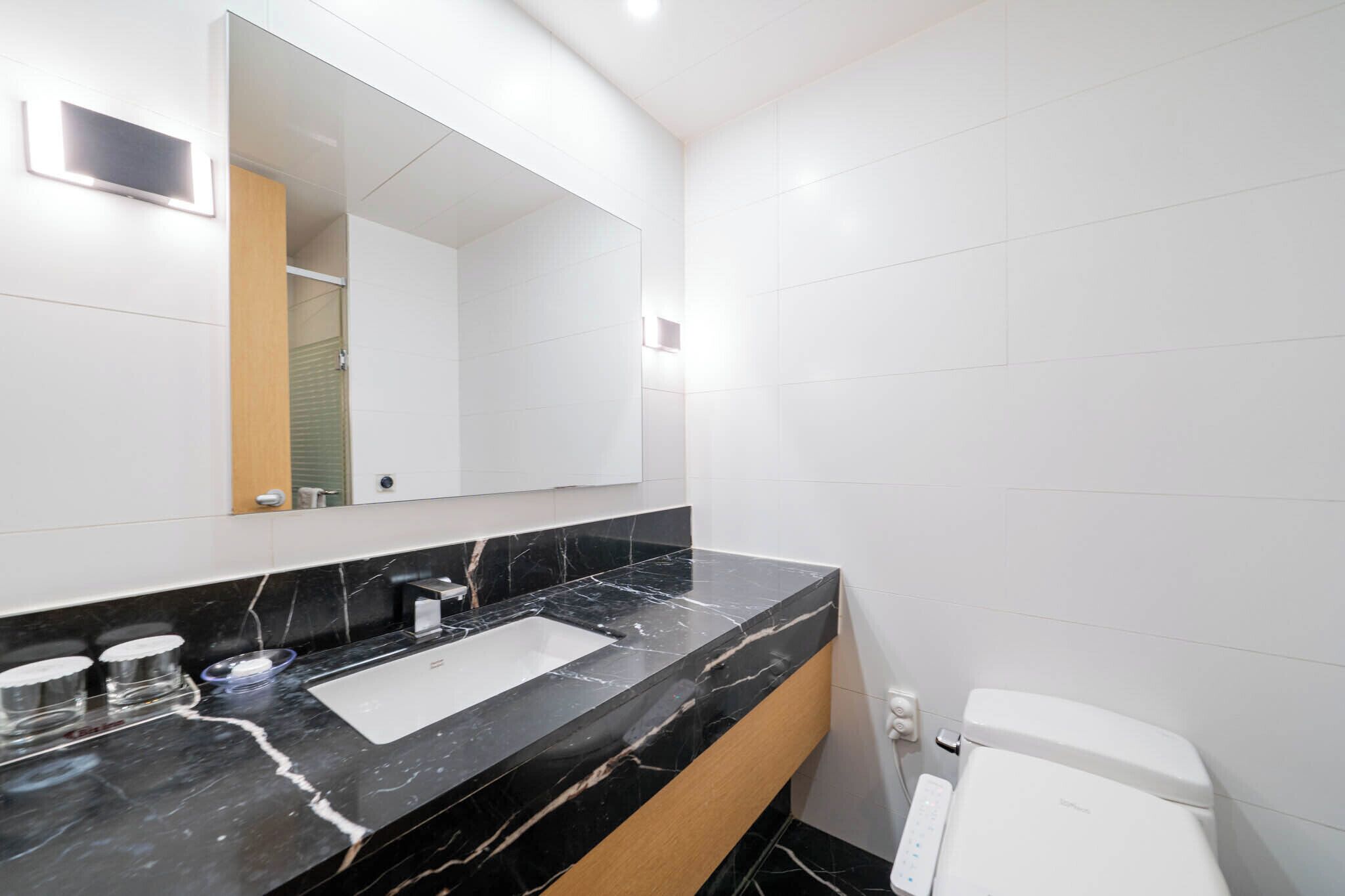 A modern bathroom with a black marble sink, a large mirror, and a white toilet.