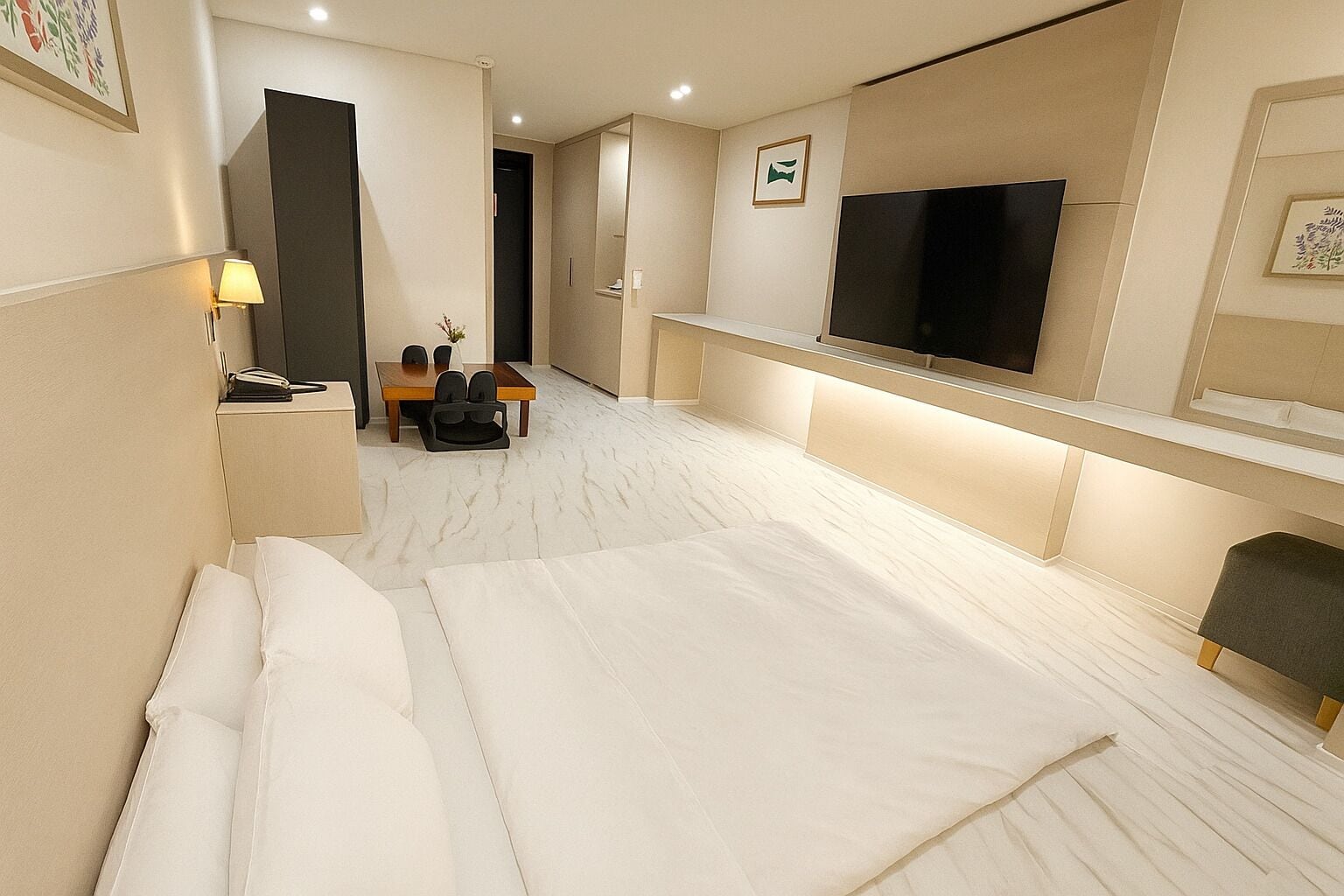 A hotel room with a large bed, a desk with chairs, a flat-screen TV, and a small table with a vase.