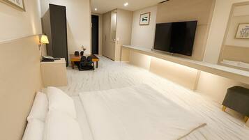 A hotel room with a large bed, a desk with chairs, a flat-screen TV, and a small table with a vase.