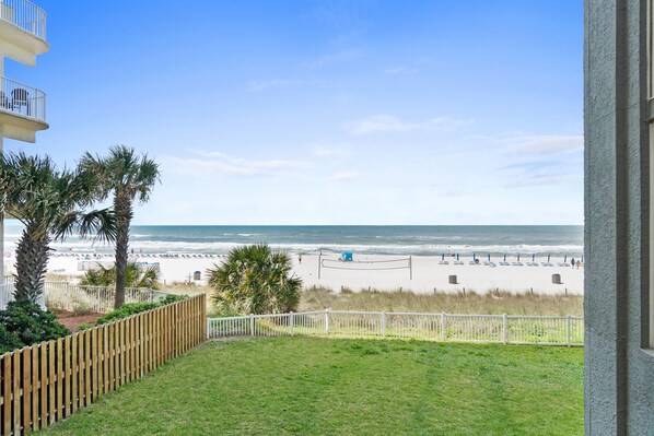 A balcony with a view of a beach, palm trees, and a wooden fence.