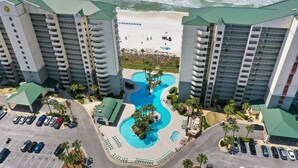 A high-rise hotel with a central swimming pool, multiple balconies, and a beach view.