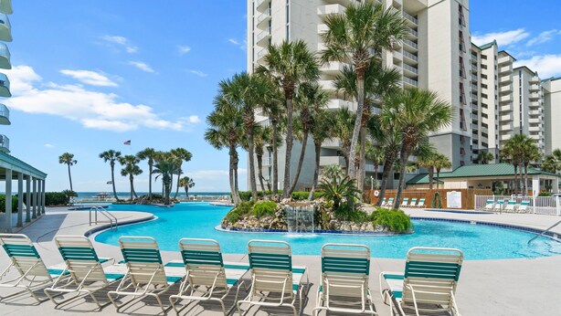 A pool area with lounge chairs, palm trees, and a building in the background.