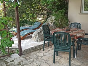 En terrasse med stenbelægning, et bord med stole og liggestole.