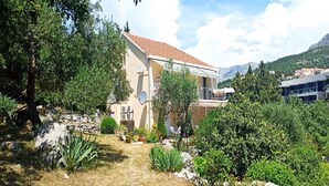 Ein zweistöckiges Haus mit rotem Ziegeldach, umgeben von üppiger Vegetation und felsigem Gelände.