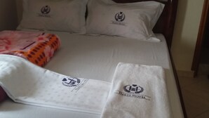 Un lit d’hôtel avec une literie blanche, une couverture rose et deux serviettes ornées du logo de l’hôtel.