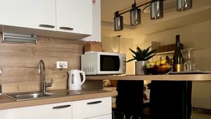 Una cocina moderna con armarios blancos, un lavamanos de acero inoxidable, un microondas y una lámpara colgante.