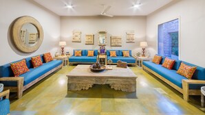 A spacious living room with blue sofas, a large mirror, and a decorative coffee table. - MANVĀR SHERGARH, THE DESERT RESORT (Shergarh)