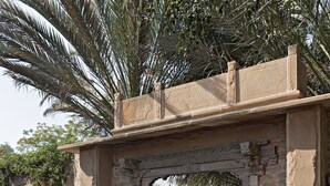 A stone archway with intricate carvings, leading to a building with a thatched roof. - MANVĀR SHERGARH, THE DESERT RESORT (Shergarh)