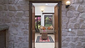 A stone-walled entrance with a wooden door, a small step leading to a seating area with cushions, and a wall-mounted light fixture. - MANVĀR SHERGARH, THE DESERT RESORT (Shergarh)