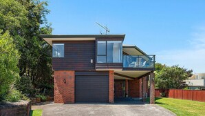 A modern two-story house with a garage, a balcony on the upper floor, and a well-maintained lawn. - Acacia Bay Getaway - Lake Taupo Holiday Home (Acacia Bay)