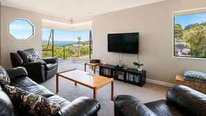 A modern living room with a large TV, leather sofas, a wooden coffee table, and a bookshelf. - Acacia Bay Getaway - Lake Taupo Holiday Home (Acacia Bay)
