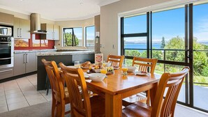 A modern kitchen with a dining area, large windows, and a view of the outdoors. - Acacia Bay Getaway - Lake Taupo Holiday Home (Acacia Bay)