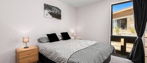 A bedroom with a bed, bedside tables, a rug, a window with curtains, and a wall-mounted picture.