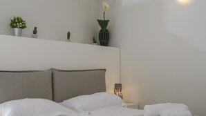 A modern hotel room with a large bed, a bedside table, a wall-mounted light, and a shelf with decorative items. - Stesicoro Exclusive House (Catania)