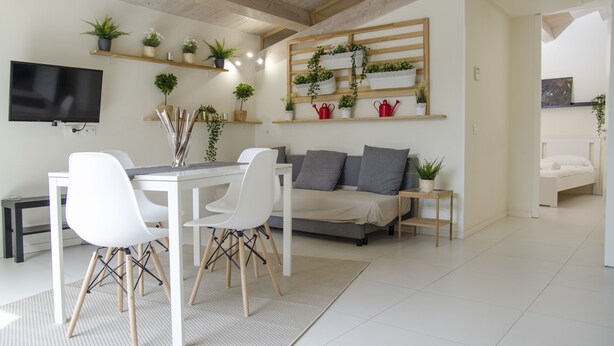 A modern living room with a dining area, a sofa, and a TV mounted on the wall. - Stesicoro Exclusive House (Catania)