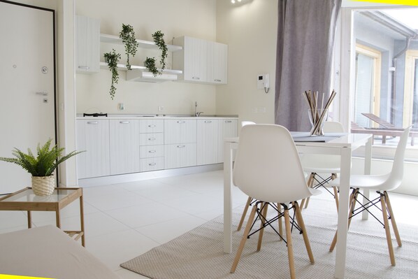 A modern kitchen with white cabinets, a dining area with white chairs, and a view of the outdoors. - Stesicoro Exclusive House (Catania)