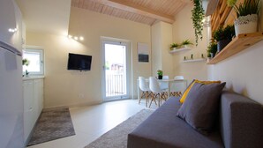 A modern living room with a sofa, a dining table with chairs, a TV mounted on the wall, and a kitchen area with cabinets and a refrigerator. - Stesicoro Exclusive House (Catania)