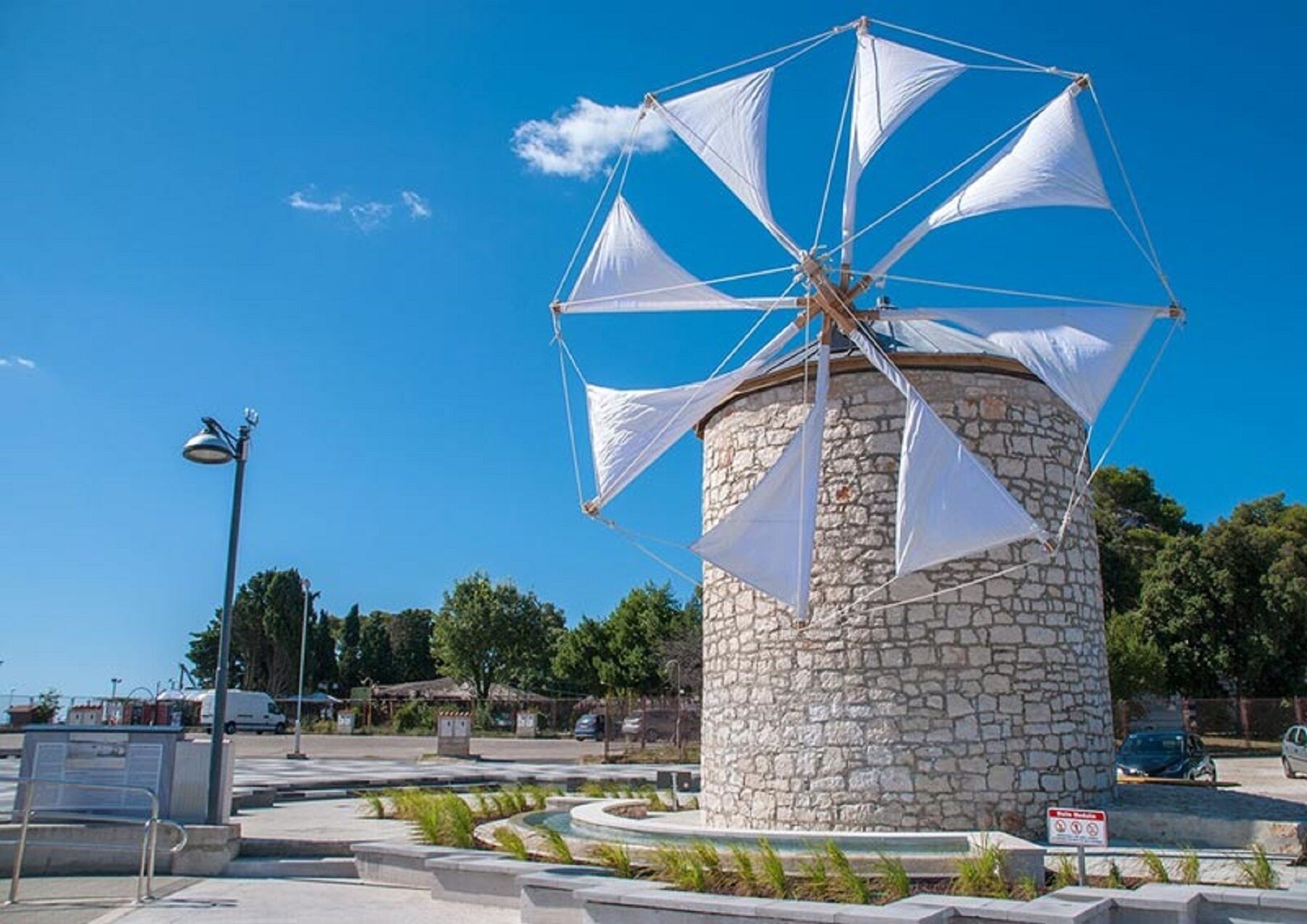 A stone windmill with white sails in a public square.