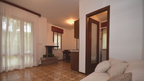 A living room with a sofa, a dining table, and a kitchen area. - Ville Annamaria (Lignano Sabbiadoro)