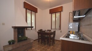 A compact kitchen with a dining area, a fireplace, and a tiled floor. - Ville Annamaria (Lignano Sabbiadoro)