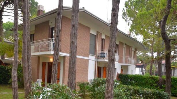A two-story building with a balcony on the second floor, surrounded by trees and greenery. - Ville Annamaria (Lignano Sabbiadoro)