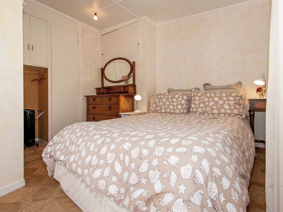 A bedroom with a large bed, a dresser, a mirror, and a nightstand with a lamp.