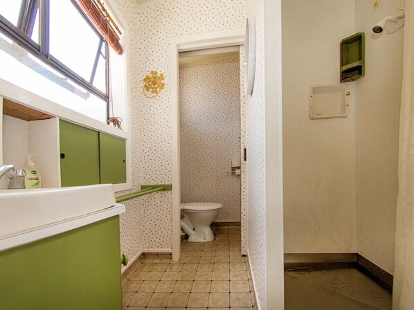 A bathroom with a toilet, green cabinets, a window, and a shower area. - Vintage Pohutukawa - Whangamata Bach (Whangamata)