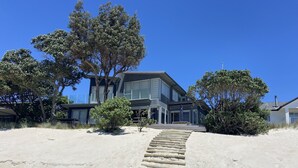 A modern house with a sandy driveway and a wooden staircase leading to the entrance. - Bliss on the Beach - Whangapoua (Whangapoua)