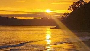A sunset over a calm body of water with a beach and hills in the background. - Bliss on the Beach - Whangapoua (Whangapoua)