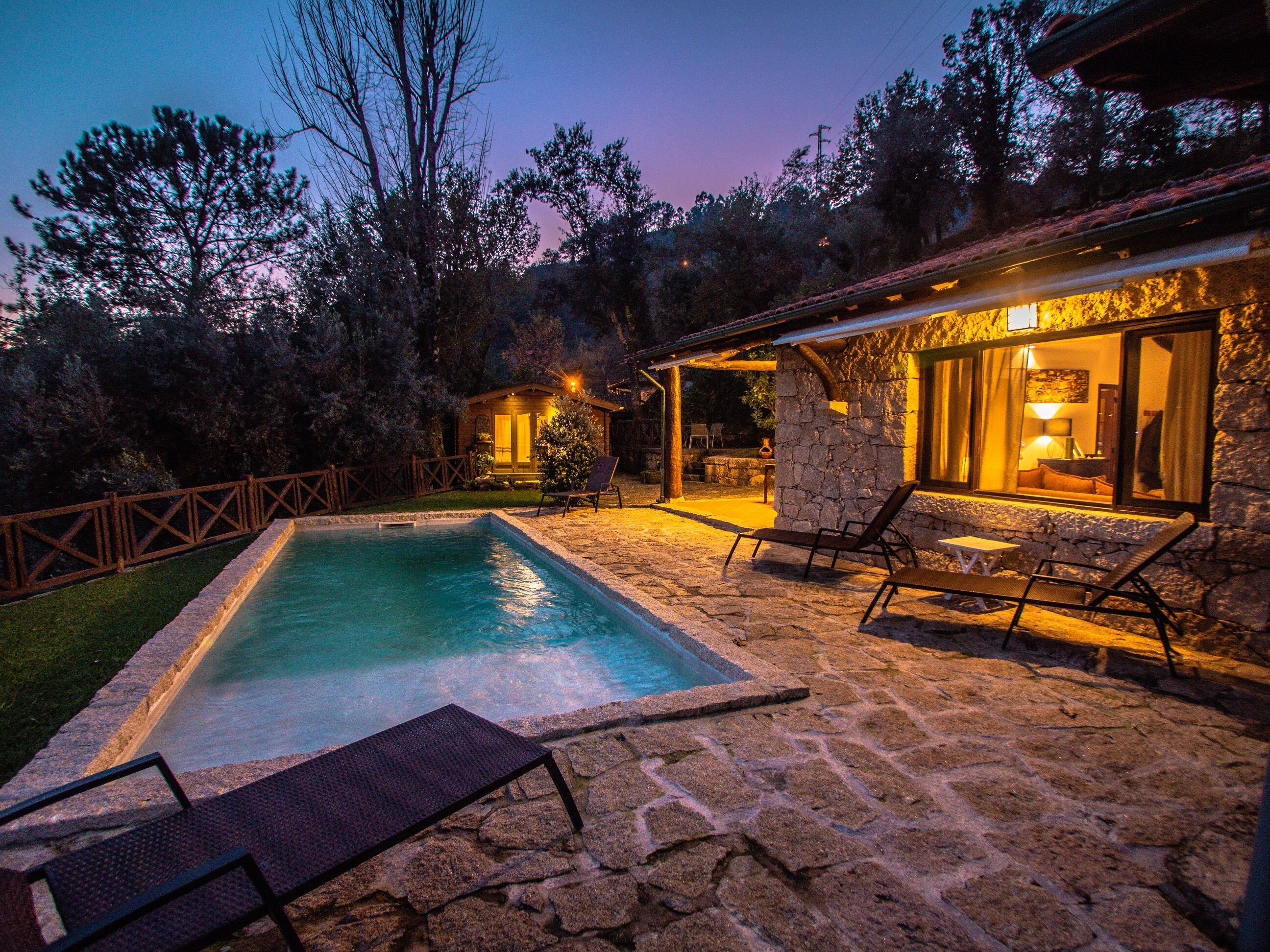 Un patio de piedra con piscina, sillas de descanso y un espacio exterior cubierto con chimenea.