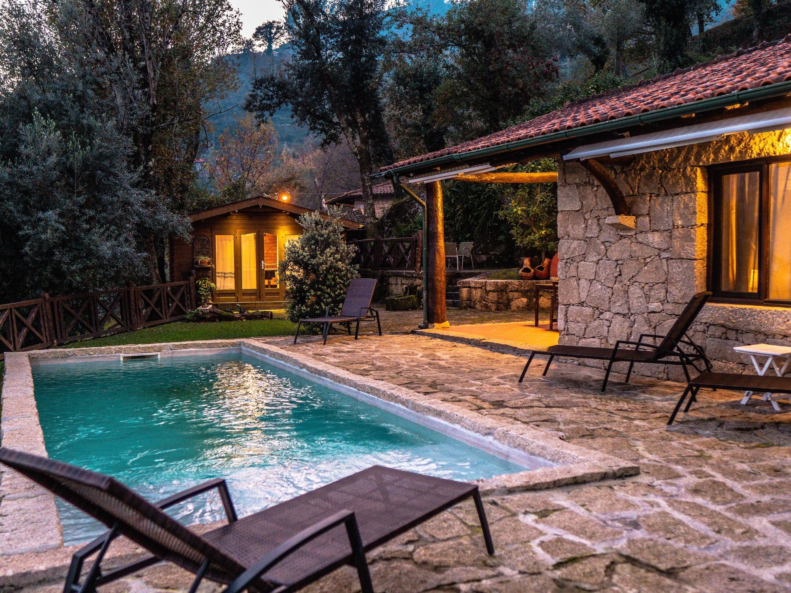 A pool area with lounge chairs, a stone patio, and a wooden cabin in the background.