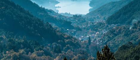 A panoramic view of a valley with a lake, surrounded by forested hills.