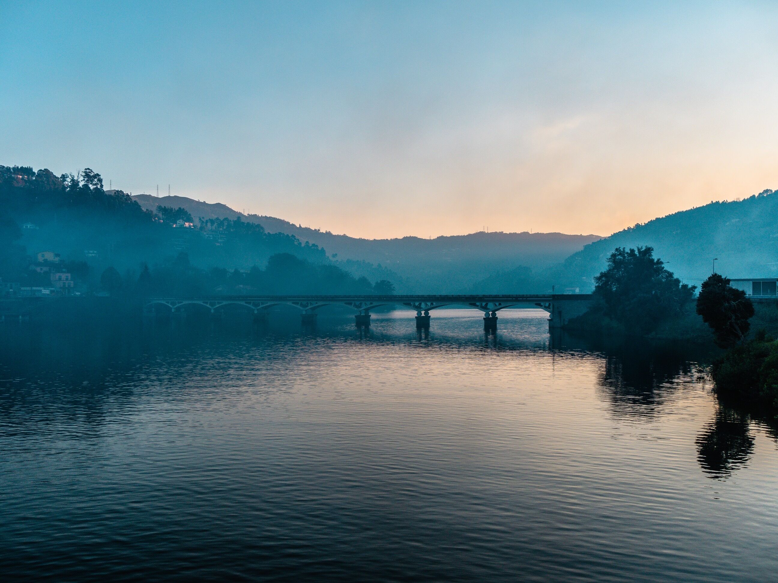 Un puente sobre un río tranquilo, con colinas al fondo.