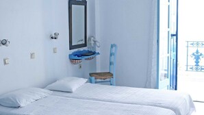 A room with two beds, a small blue chair, a mirror, and a window with a view. - Daidalos Hotel (Ikaria)