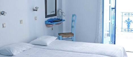 A room with two beds, a small blue chair, a mirror, and a window with a view.