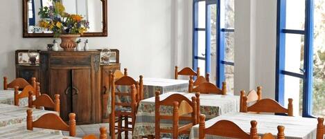 Un comedor con mesas y sillas de madera, un espejo y un florero sobre un mueble.