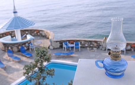 A poolside view with a clear view of the ocean, a lounge area with blue chairs, and a decorative glass lamp.
