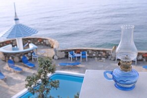 Vista a la piscina con una clara vista del océano, un área de descanso con sillas azules y una lámpara de vidrio decorativa.