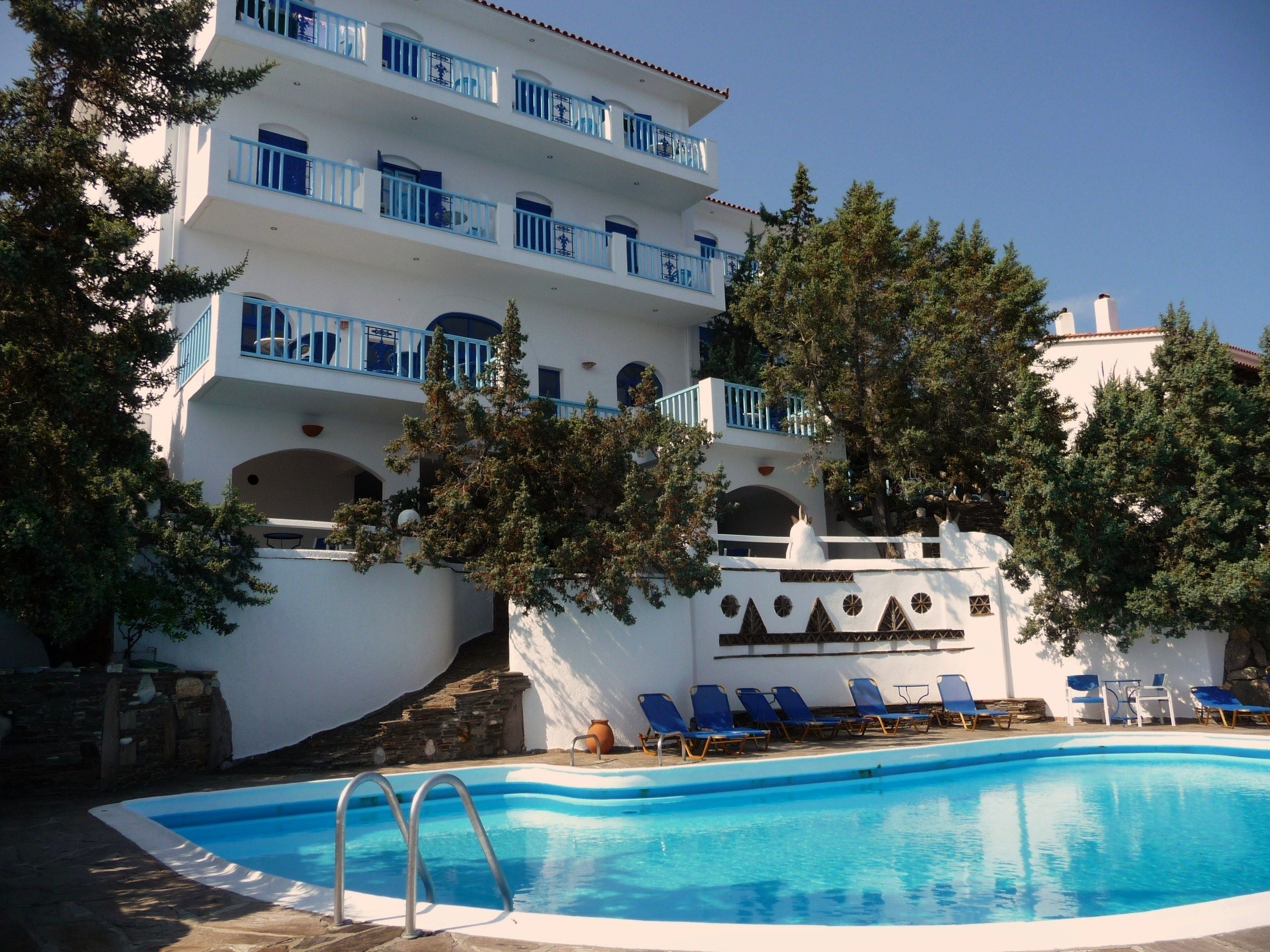 A multi-story hotel with a swimming pool, outdoor seating, and trees.