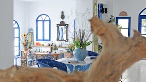 A dining area with a white table, blue chairs, and a large vase of flowers. - Daidalos Hotel (Ikaria)