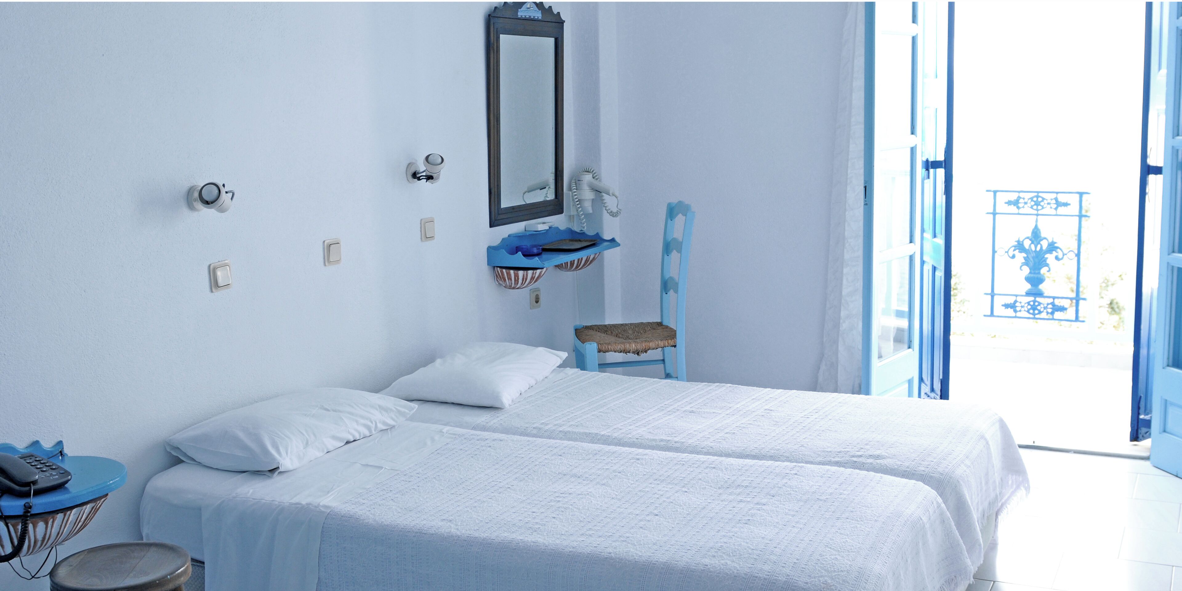 Quarto com duas camas, um espelho, um telefone e um banquinho.