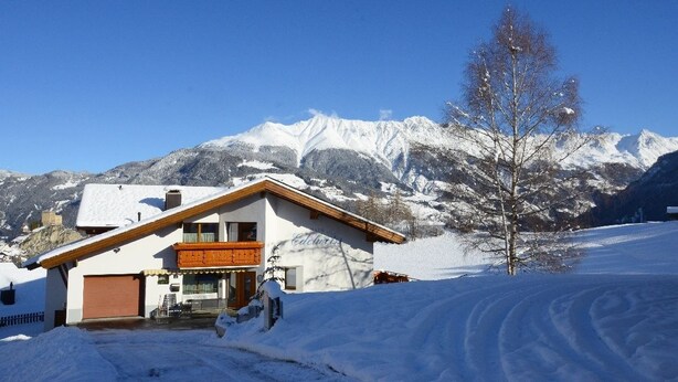 A snow-covered mountain landscape with a building featuring a wooden balcony and a garage. - Edelweiss Ladis (Ladis)