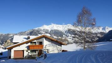 A snow-covered mountain landscape with a building featuring a wooden balcony and a garage.