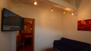 A living room with a dark blue sofa, a flat-screen TV mounted on the wall, a red artwork, and a string of lights. - Edelweiss Ladis (Ladis)