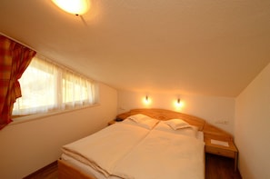 A bedroom with a bed, a nightstand, a window with curtains, and wall-mounted lights. - Edelweiss Ladis (Ladis)